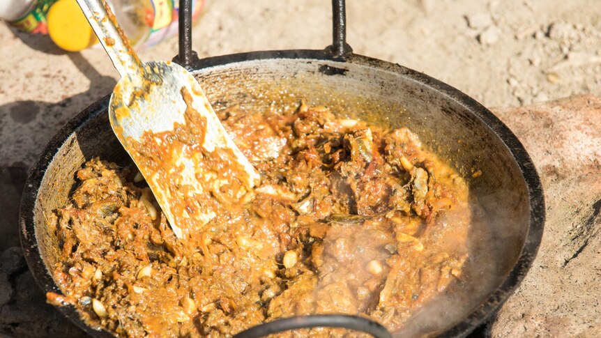 Frying fish in chutney ingredients over outdoor fire, Bangladesh