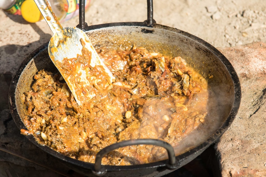 Frying fish in chutney ingredients over outdoor fire, Bangladesh