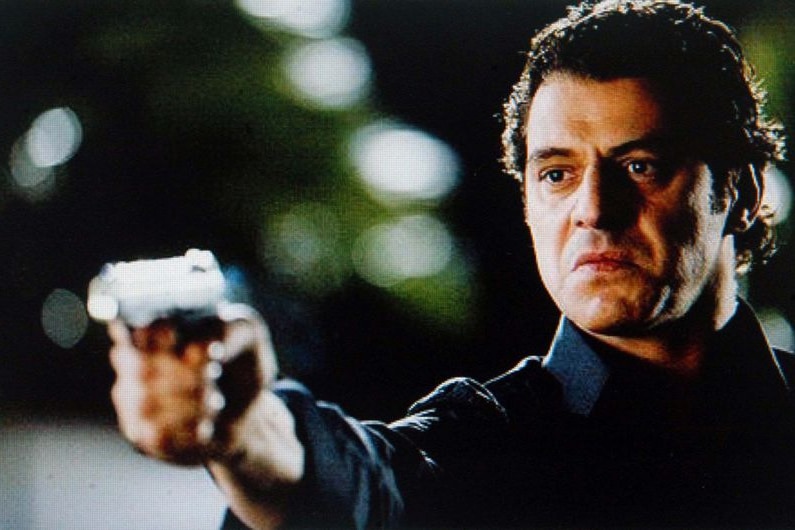 Vince Colosimo, in character as Carlton Crew gangster Alphonse Gangitano, stands with gun drawn.