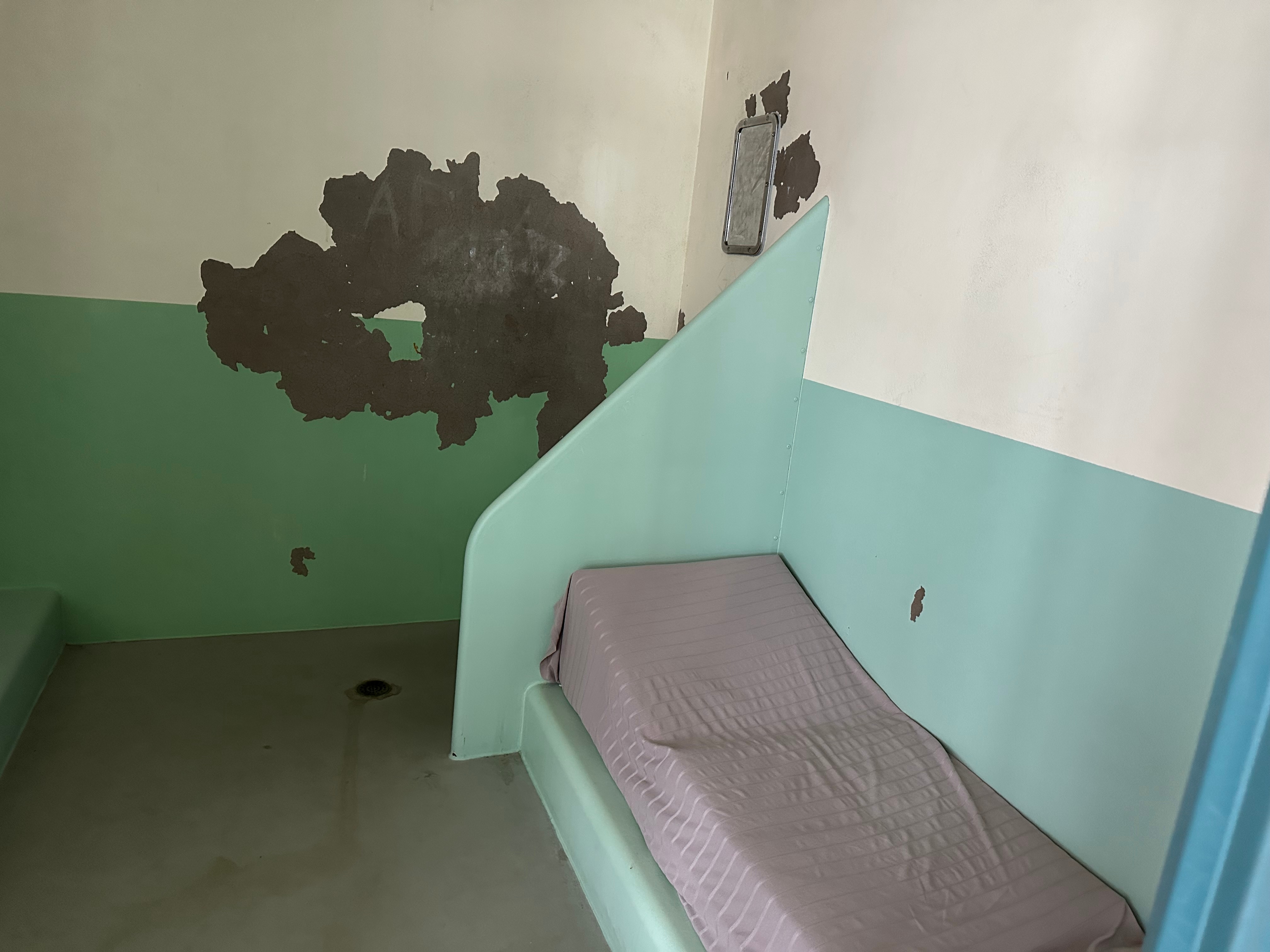 Inside a dingy watch-house cell with paint scrapped of the walls. 