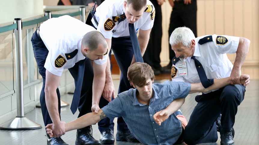 A protester lies on the ground with three security guards holding his arms outstretched.
