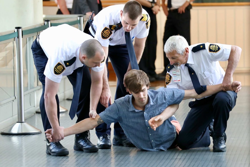 A protester lies on the ground with three security guards holding his arms outstretched.