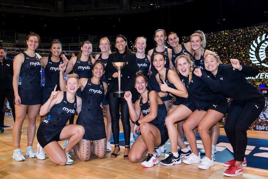 A group of netball players knelt and stood smiling on the field holding the Constellation Cup.