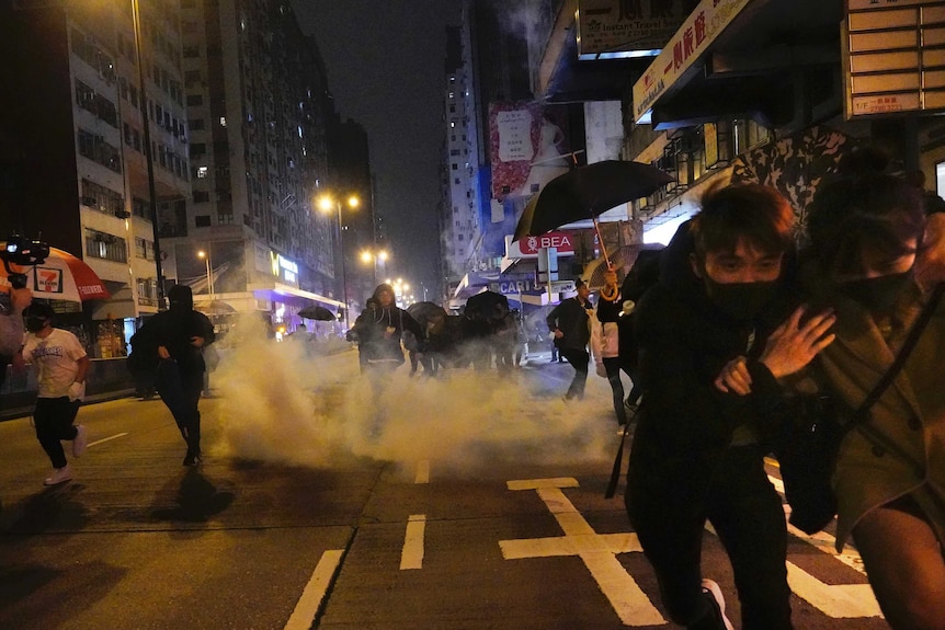 On a street in Hong Kong people duck and run as a cloud of tear gas emerges in the background.