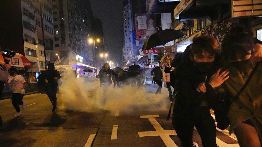 On a street in Hong Kong people duck and run as a cloud of tear gas emerges in the background.