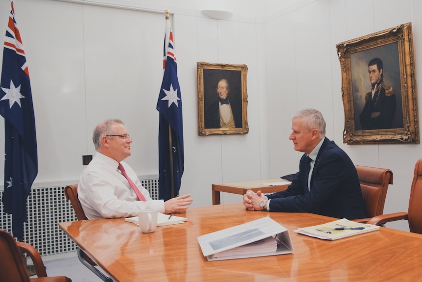 Scott Morrison (l) and Michael McCormack (r) sit talking at a table with Australian flags and portraits decorating the room