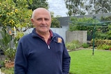 A man with white hair stands in his backyard with a letter in his hand