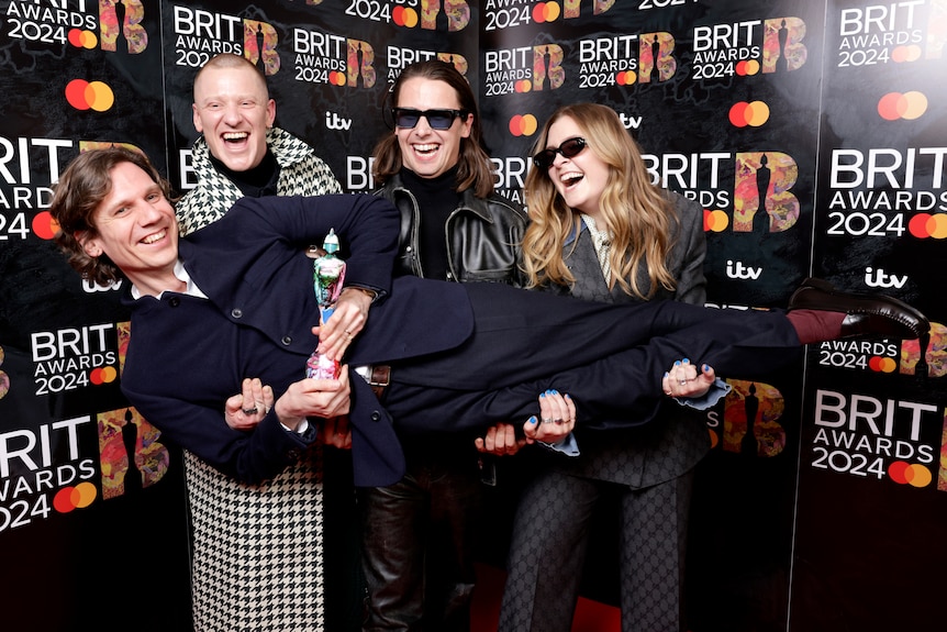 Three men and a woman hold up another man holding the BRIT award