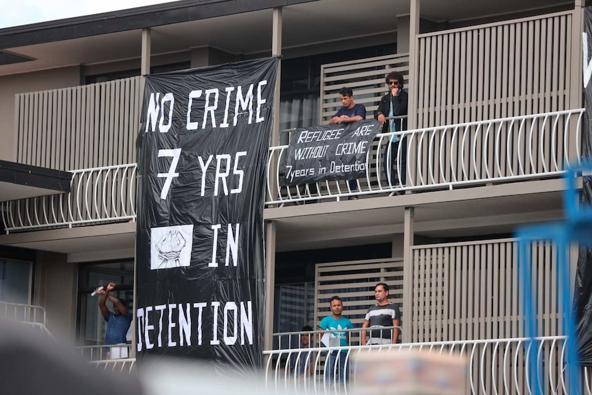 Men stand on the balcony of an apartment block where hanging signs read "no crime 7 yrs in detention".