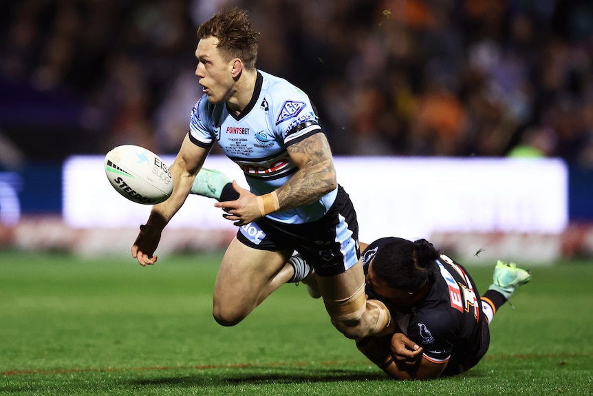A Cronulla NRL player passes the ball to his right against Wests Tigers.