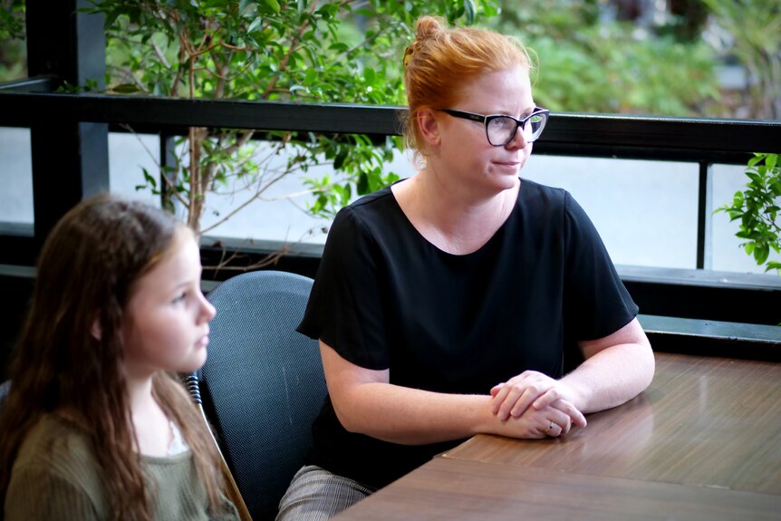A woman with red hair sits at a cafe table with a young child next to her