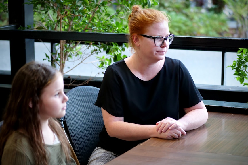 A woman with red hair sits at a cafe table with a young child next to her