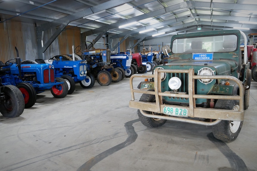 Photo of an old blue Jeep and tractors in a shed.