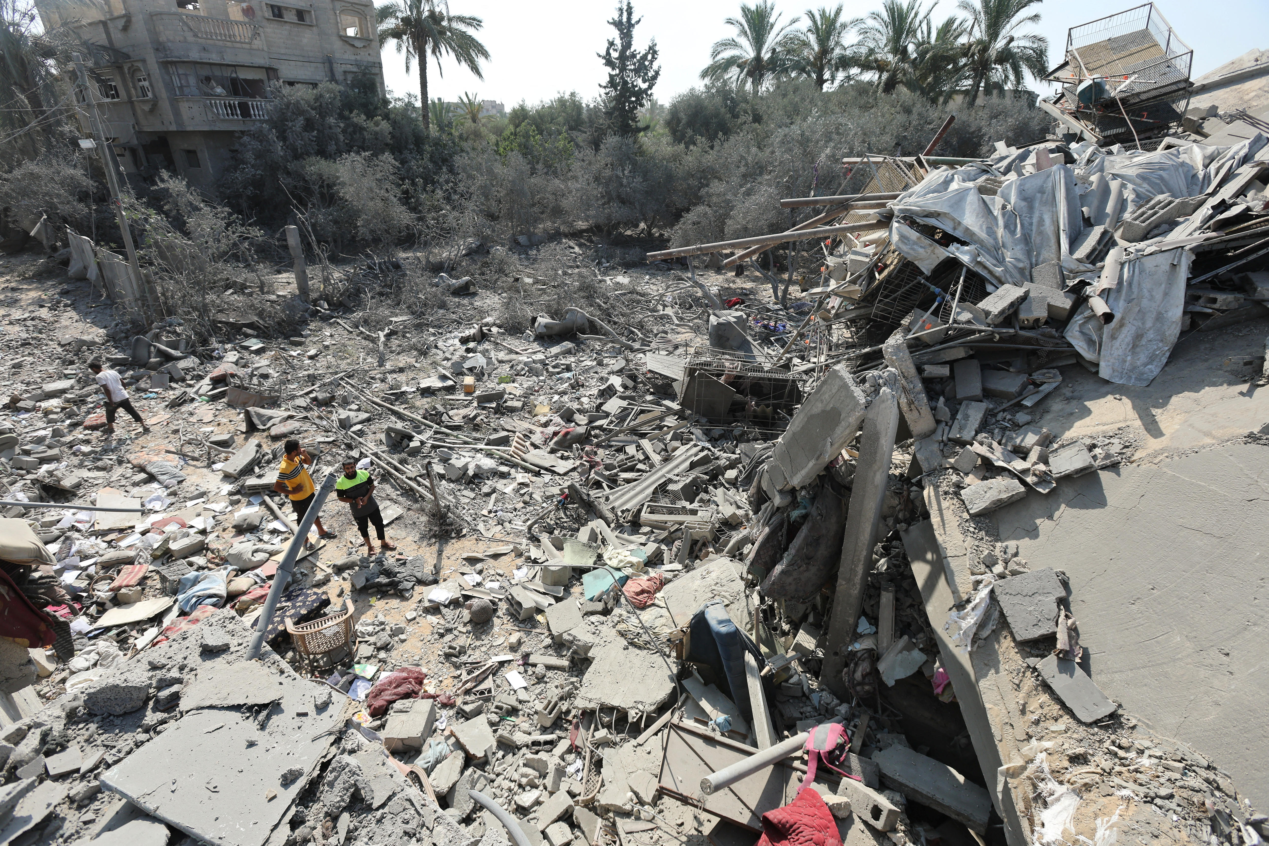 Three men inspect the rubble of a multi-storey concrete house that was hit in an airstrike, palm trees in the background