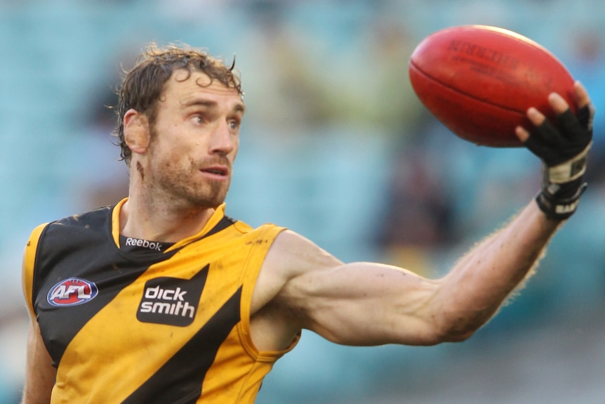 Man holding an AFL ball in his hand.