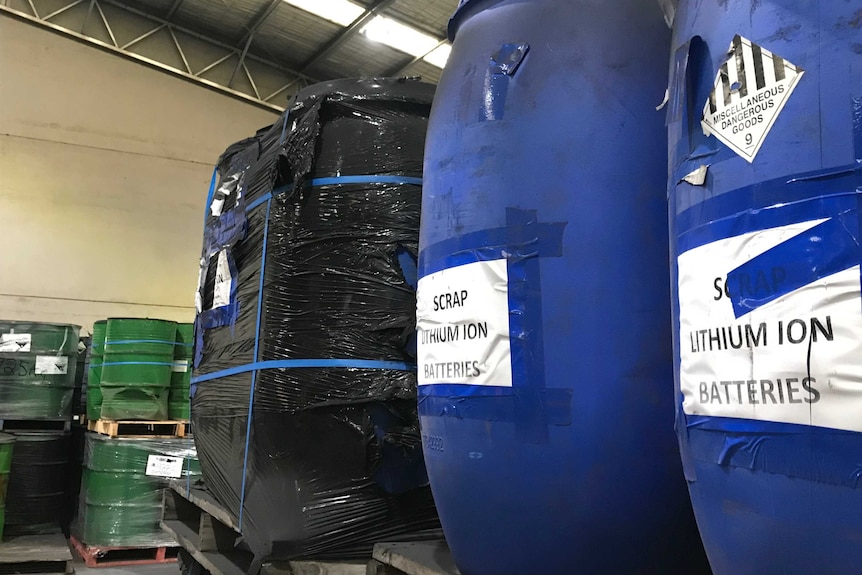 Blue plastic drums full of batteries await recycling inside a factory.
