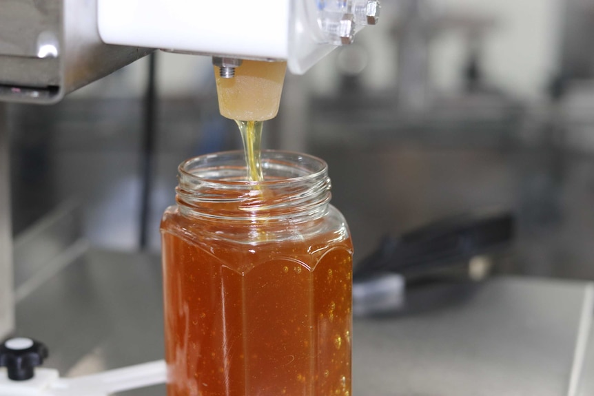 A jar of honey is filled using an automatic dispenser