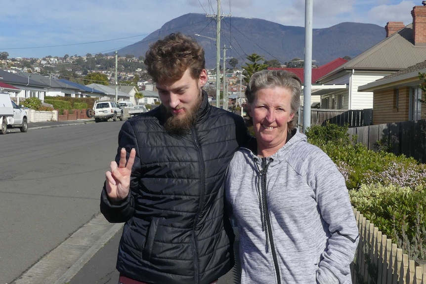 Angela Wilton with her 21-year-old son standing on a suburban Hobart street with kunanyi/Mount Wellington in the background