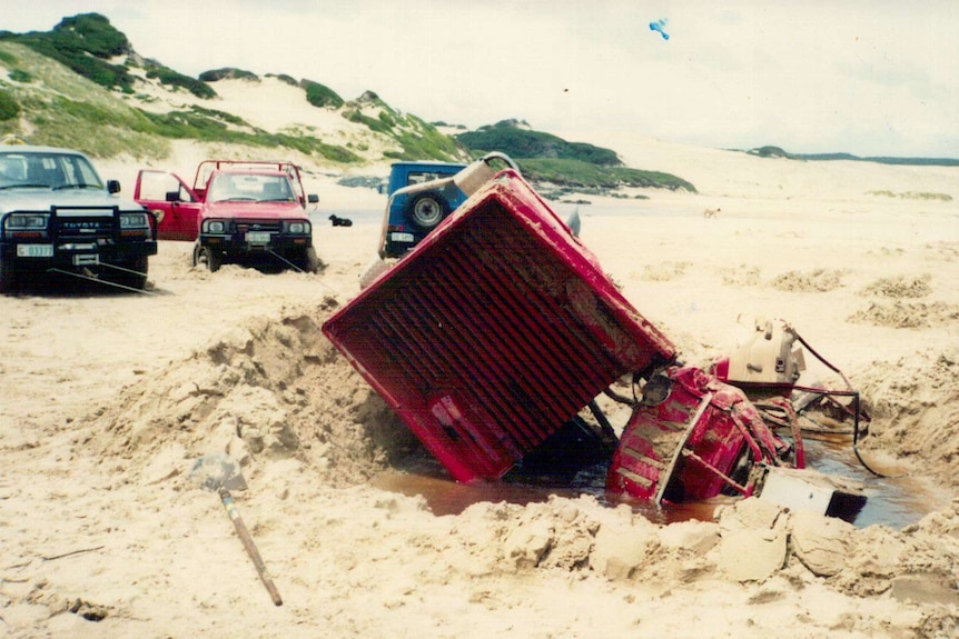 A red hilux ute that's been pulled to bits by other vehicles that have tried to winch it out of sand.