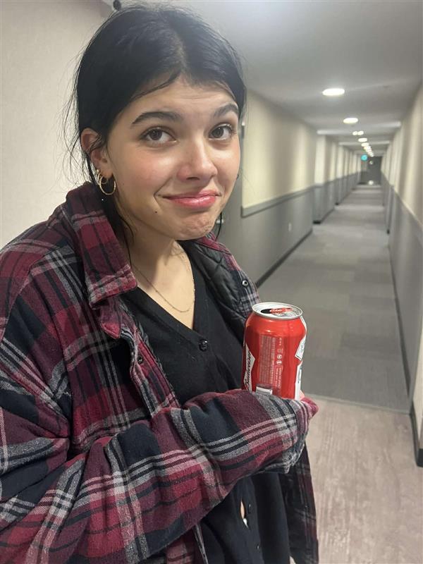 Una mujer joven hace una expresión divertida a la cámara mientras sostiene una lata de refrescos.