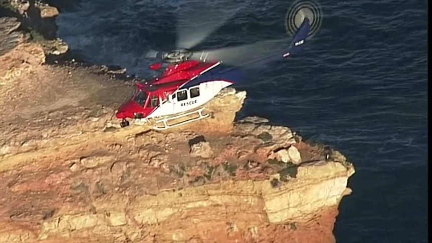 A red helicopter hovering above a cliff face