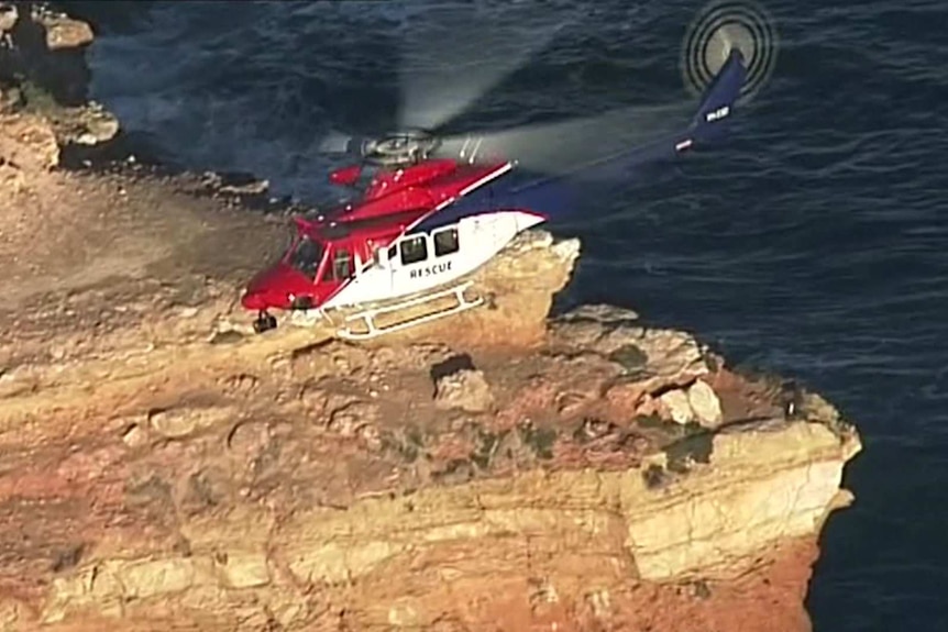 A red helicopter hovering above a cliff face