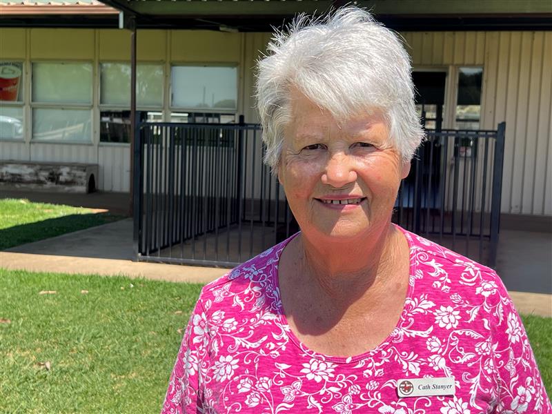Older woman with short grey hair stands outside a building smiling.
