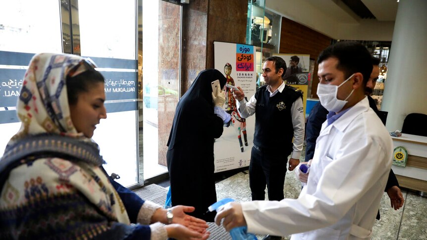 Iranian women being tested for temperature by men wearing face masks.
