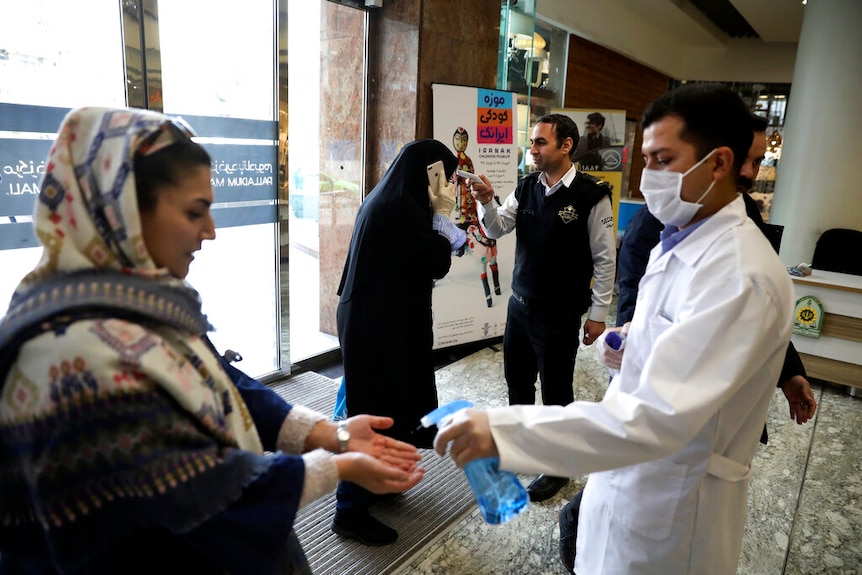 Iranian women being tested for temperature by men wearing face masks.