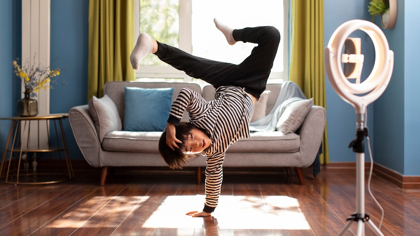 Photo of a young Asian boy break dancing in his living room in front of a camera and ring light. 