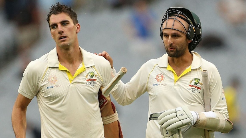 Pat Cummins carries his bat under one arm and his helmet in the other while Nathan Lyons pats his shoulder.