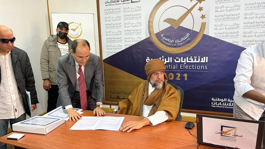 Saif al-Islam Gaddafi seated at a desk with a grey beard as he registers as presidential candidate, Nov 12, 2021.