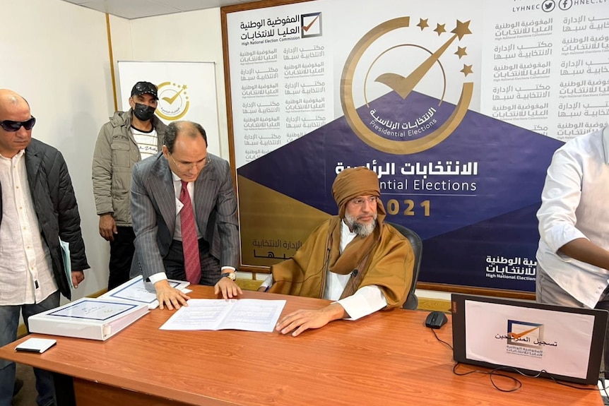 Saif al-Islam Gaddafi seated at a desk with a grey beard as he registers as presidential candidate, Nov 12, 2021.