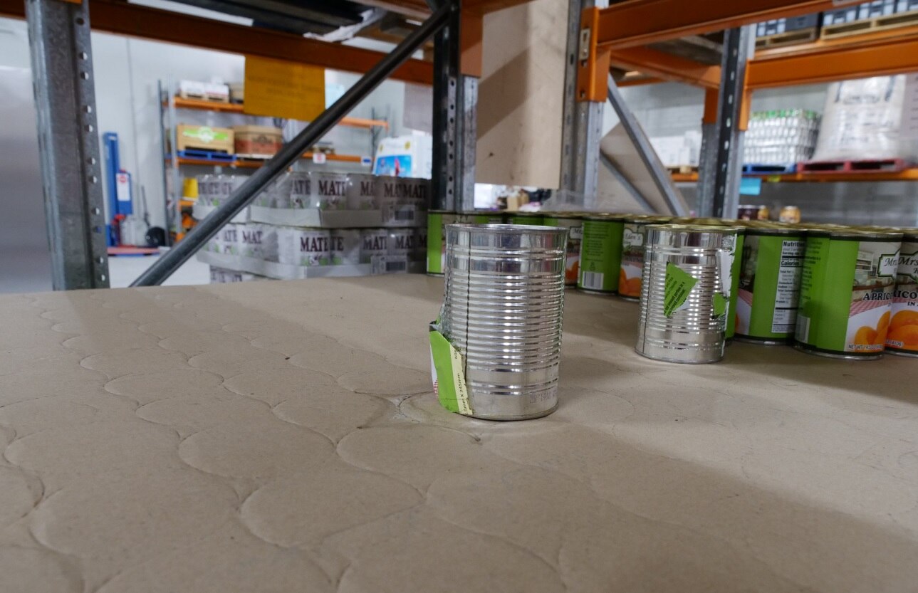 A close-up of an empty shelf with a few cans.