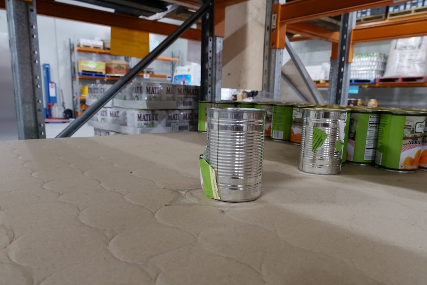 A close-up of an empty shelf with a few cans.