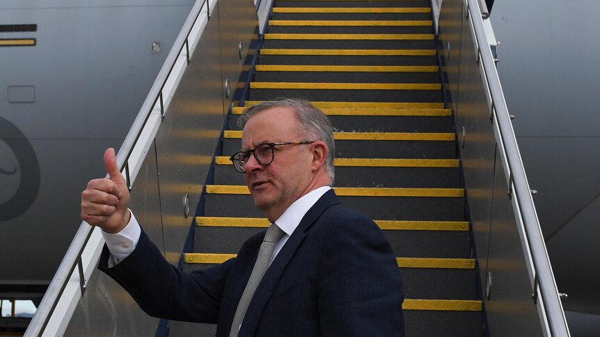 anthony albanese gives a thumbs up at the bottom of a set of plane stairs
