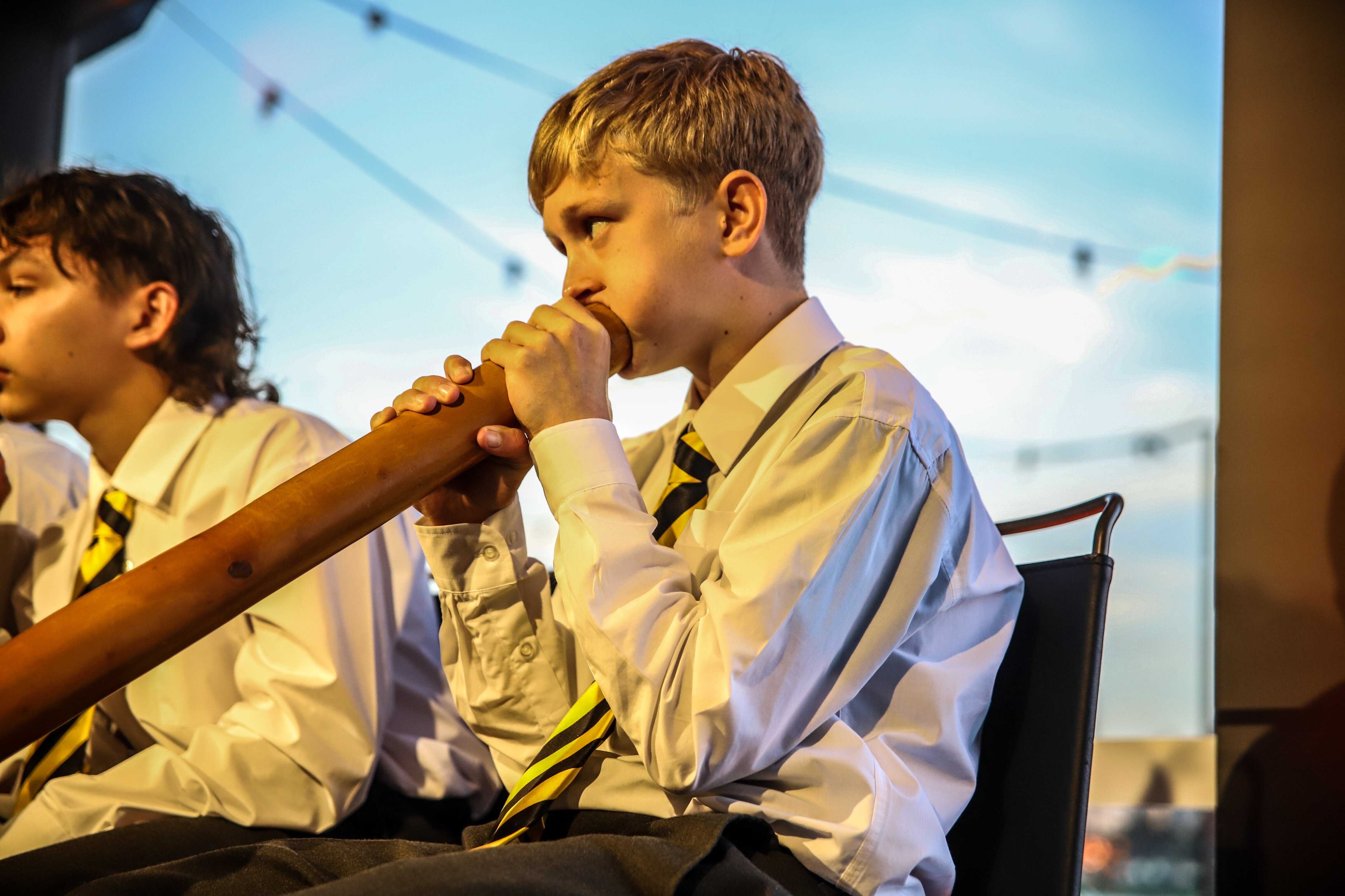Malakai plays the yidaki at a performance wearing a suit and tie