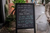 A man walks past a chalkboard advertising a restaurant's opening hours and diner numbers.