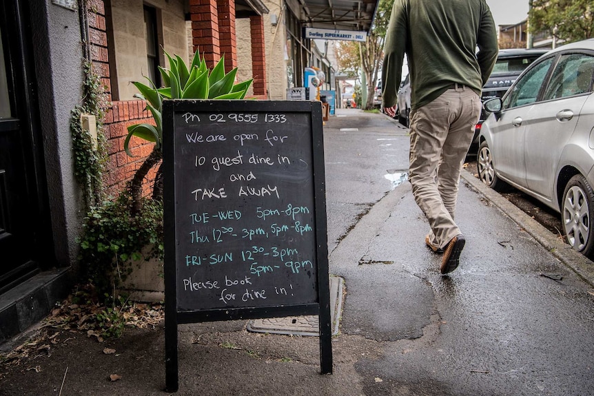 A man walks past a chalkboard advertising a restaurant's opening hours and diner numbers.