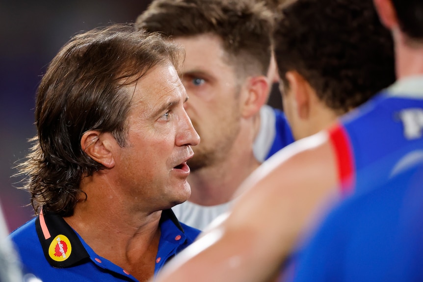 Luke Beveridge speaks to Western Bulldogs players on the field during an AFL game.