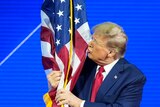 Donald Trump kisses the American flag on stage at a conference