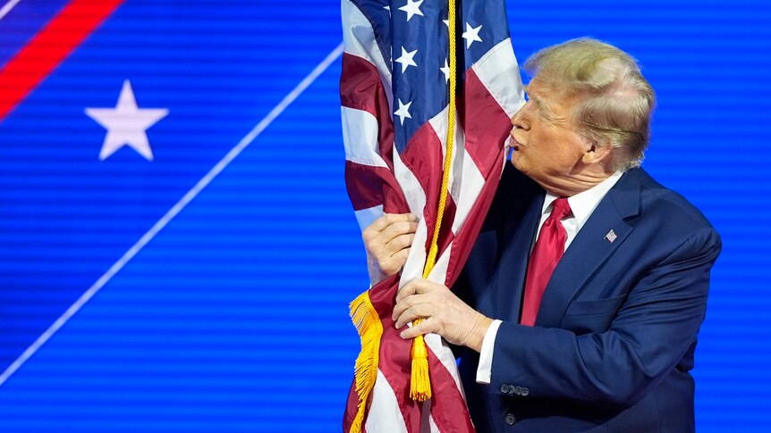 Donald Trump kisses the American flag on stage at a conference