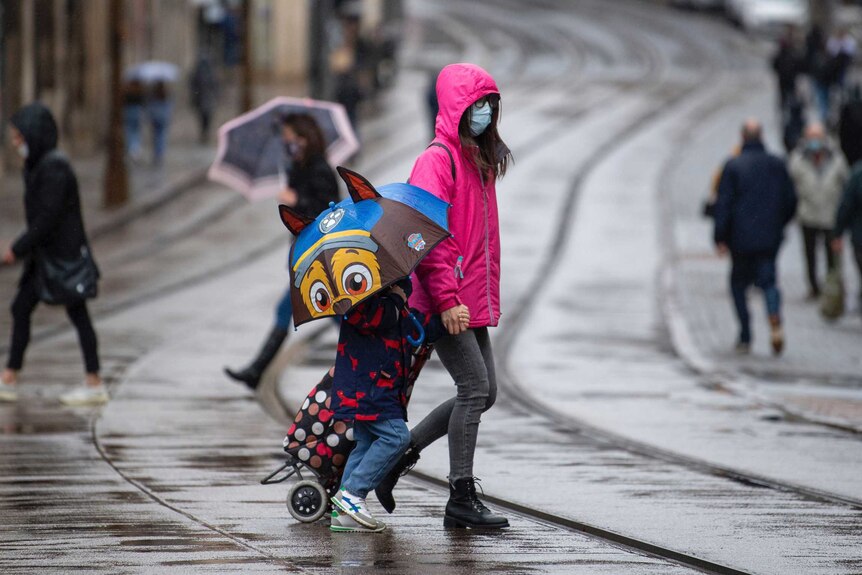 Many people wearing face masks as they move along a shopping street as rain falls in Nottingham.