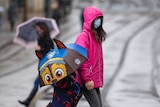 Many people wear face masks as they move along a shopping street as rain falls in Nottingham.