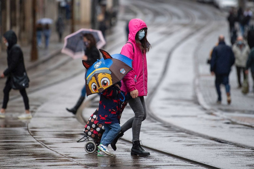 Many people wear face masks as they move along a shopping street as rain falls in Nottingham.