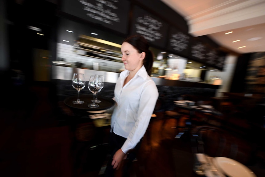 A waitress in a white shirt carries a tray of glasses