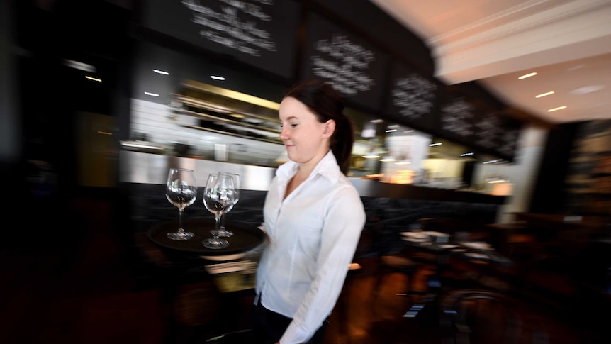 A waitress in a white shirt carries a tray of glasses.