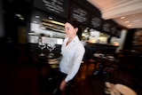 A waitress in a white shirt carries a tray of glasses in a Canberra restaurant.