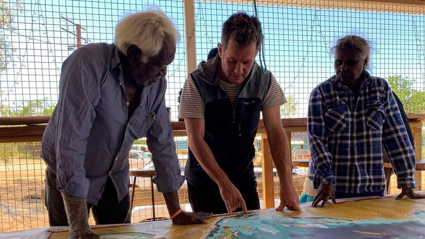 Three people talking stand looking over a map of the Limmen Bight area.