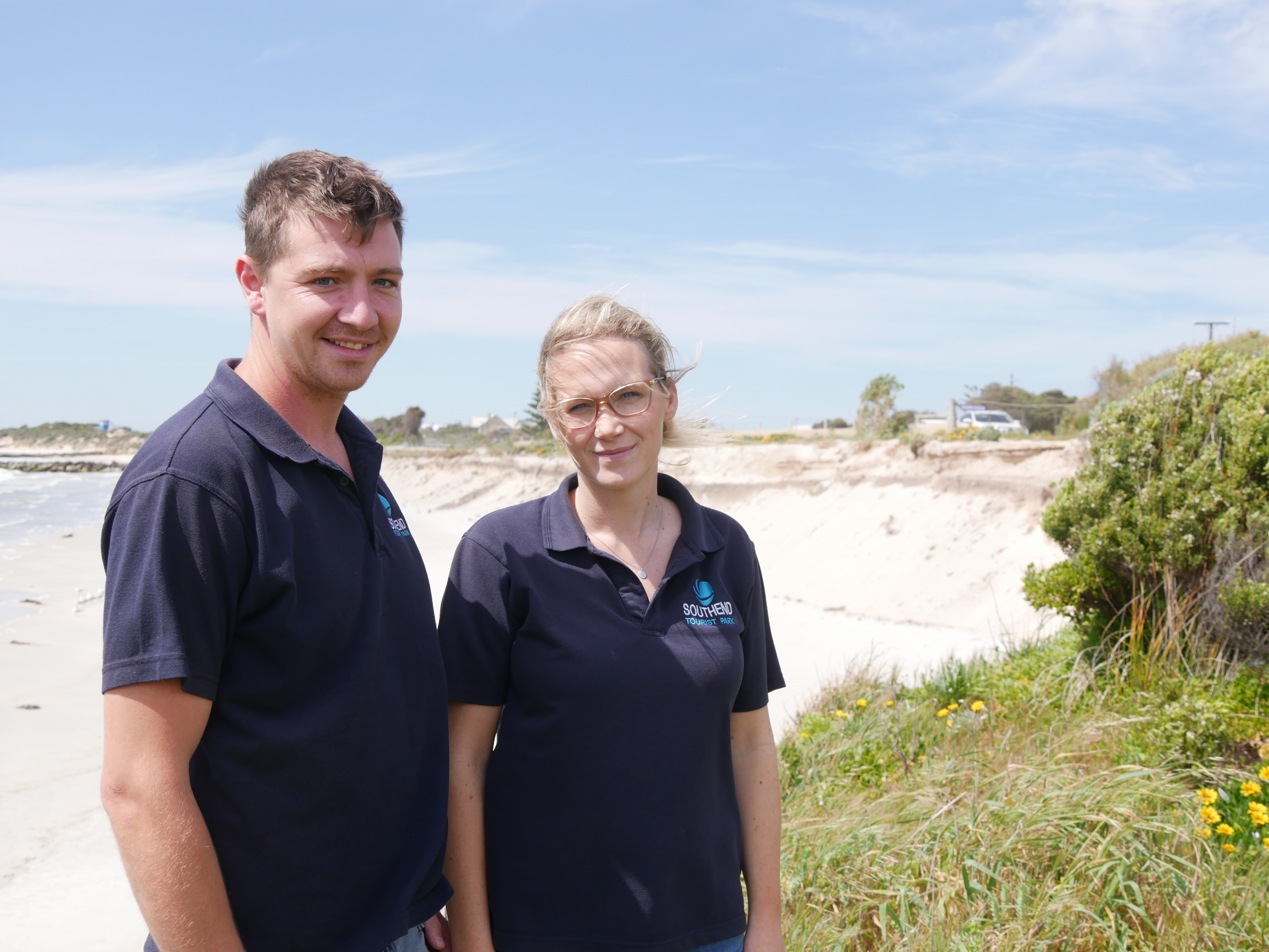 A man and woman standing next to a beach. 